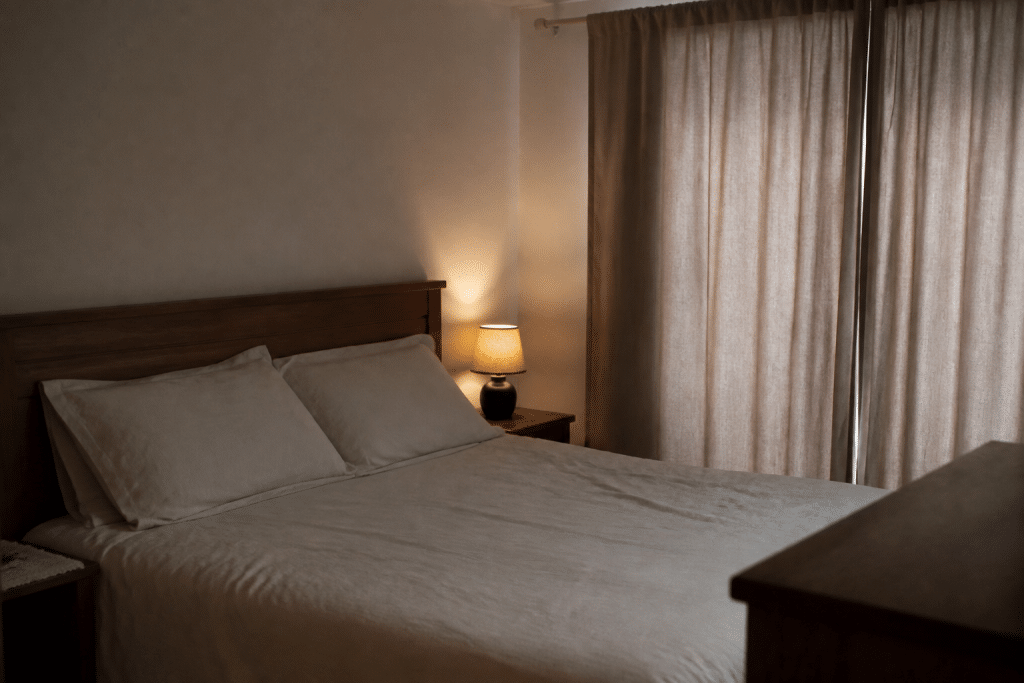 Chambre apaisante avec lit fait, lampe tamisee et rideau ferme