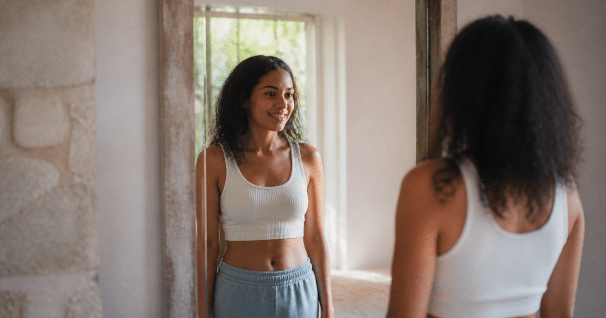 Femme souriante debout face au miroir, bras detendus le long du corps