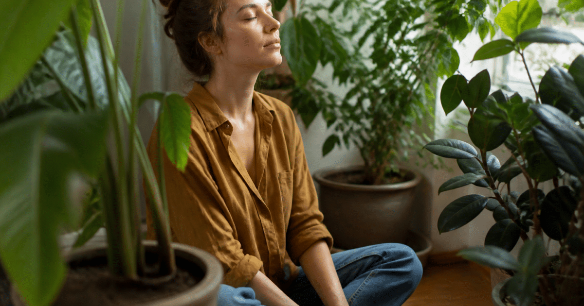 Femme assise au sol respirant profondément pres plantes vertes