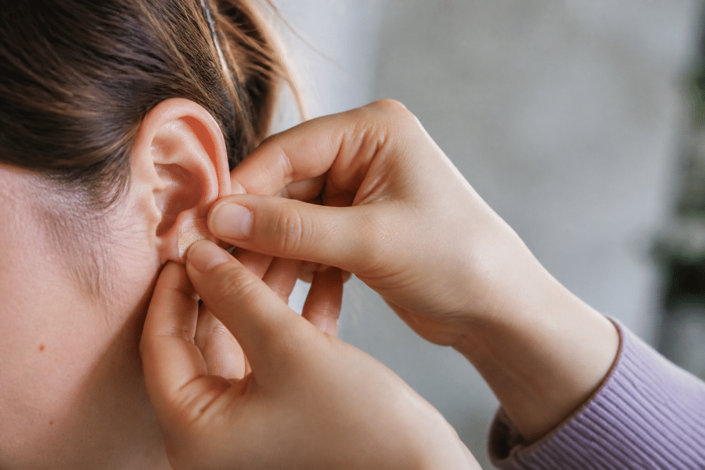 Mains appliquant petit pansement chair sur lobe oreille propre