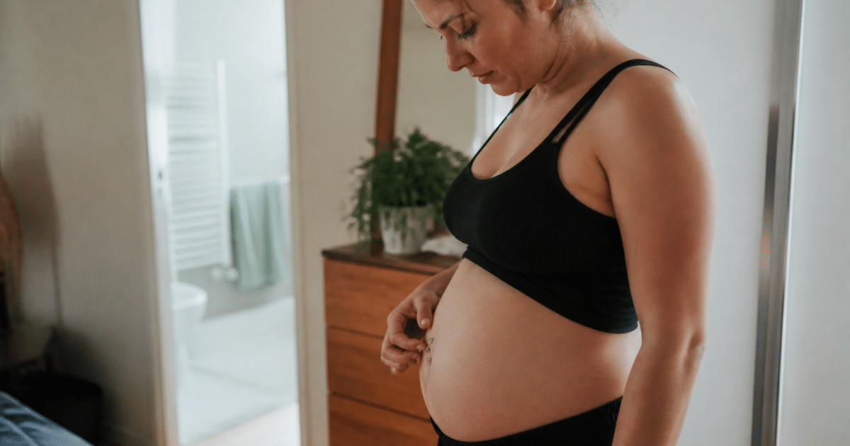 Femme enceinte de profil touchant son piercing au nombril