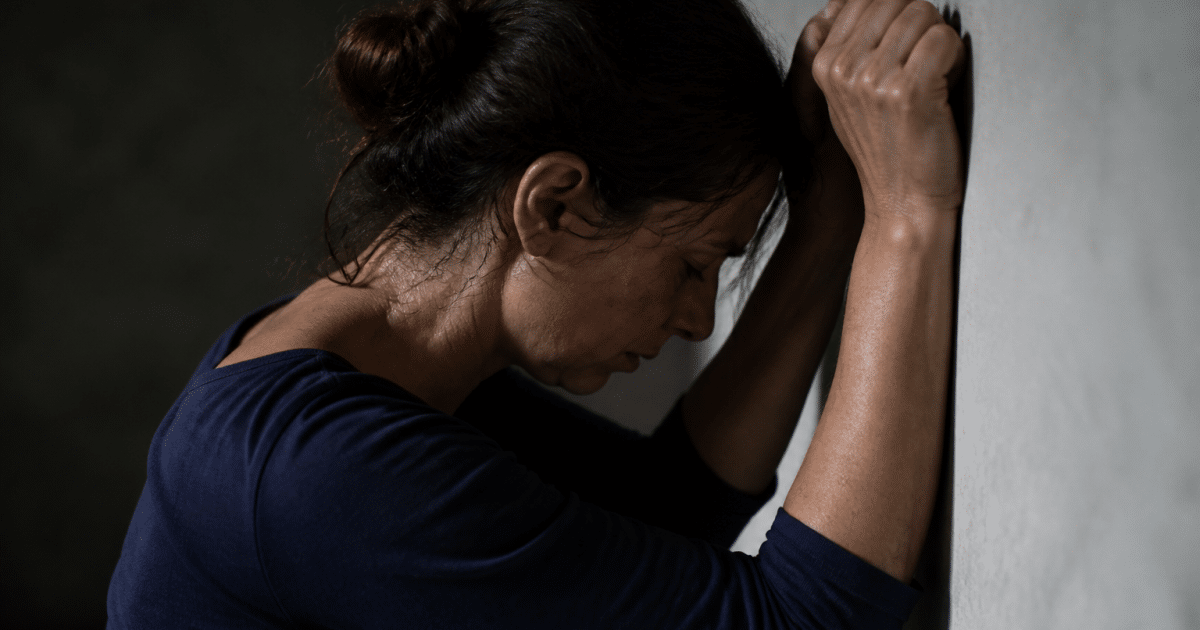 Visage tendu dans l'ombre, mains crispees contre le mur