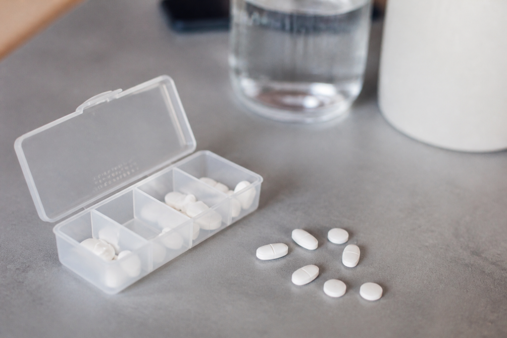 Pilulier ouvert avec pilules blanches sur table grise