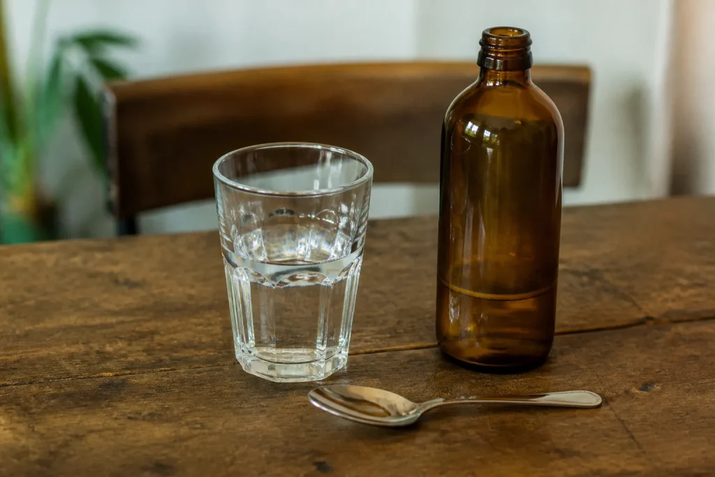 Verre d'eau, cuillere et bouteille ambree sur table